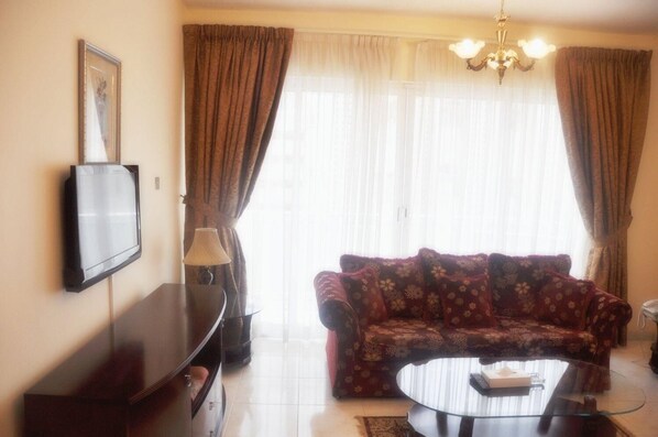 A living room with a sofa, a TV, a lamp, and a chandelier.