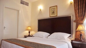 A hotel room with a large bed, a bedside table with a lamp, a framed picture on the wall, and a door. - Royal Plaza Hotel Apartments (Dubai)