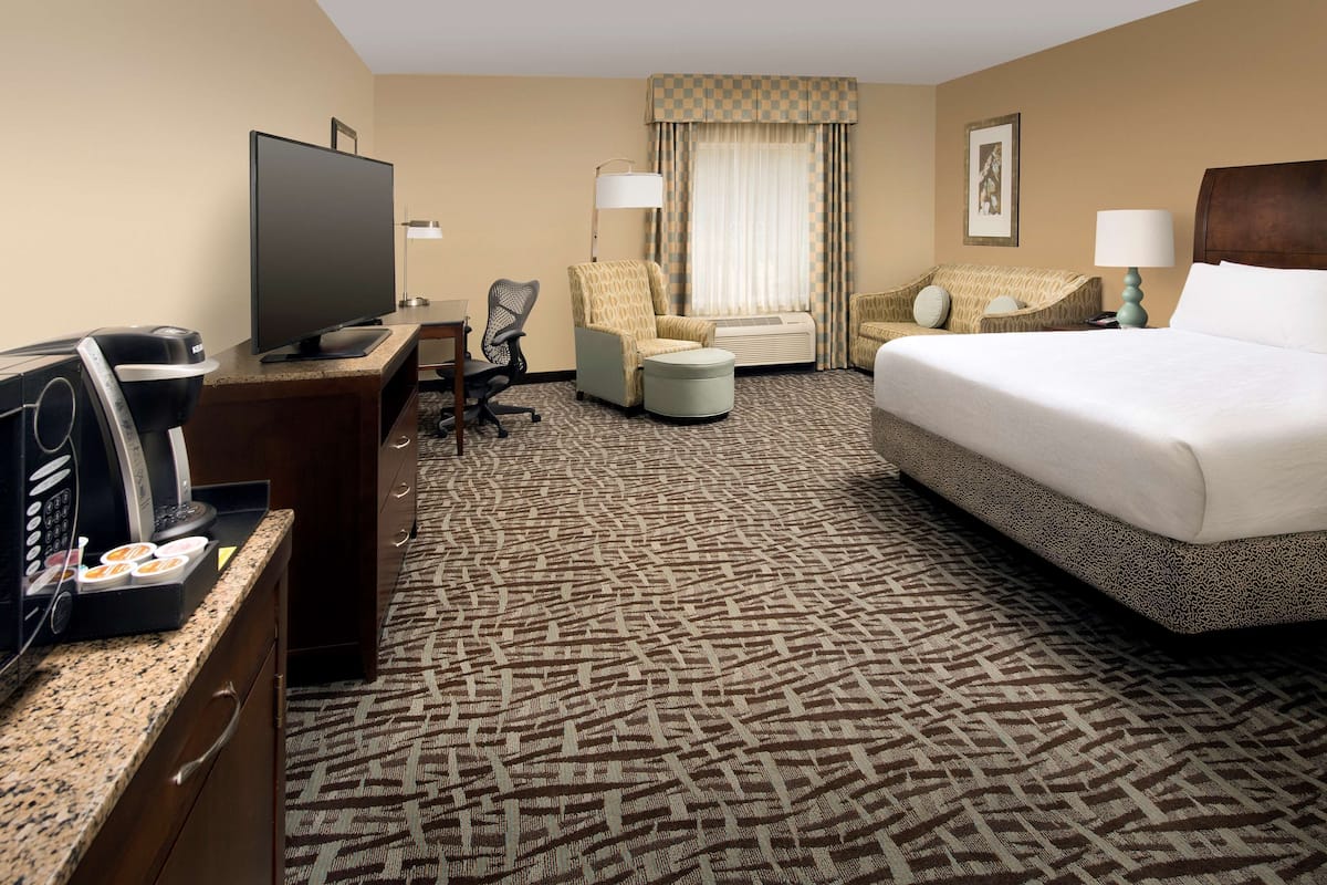 Een hotelkamer met een bed, een bureau met een televisie, een stoel, een bank en een vloerbedekking.