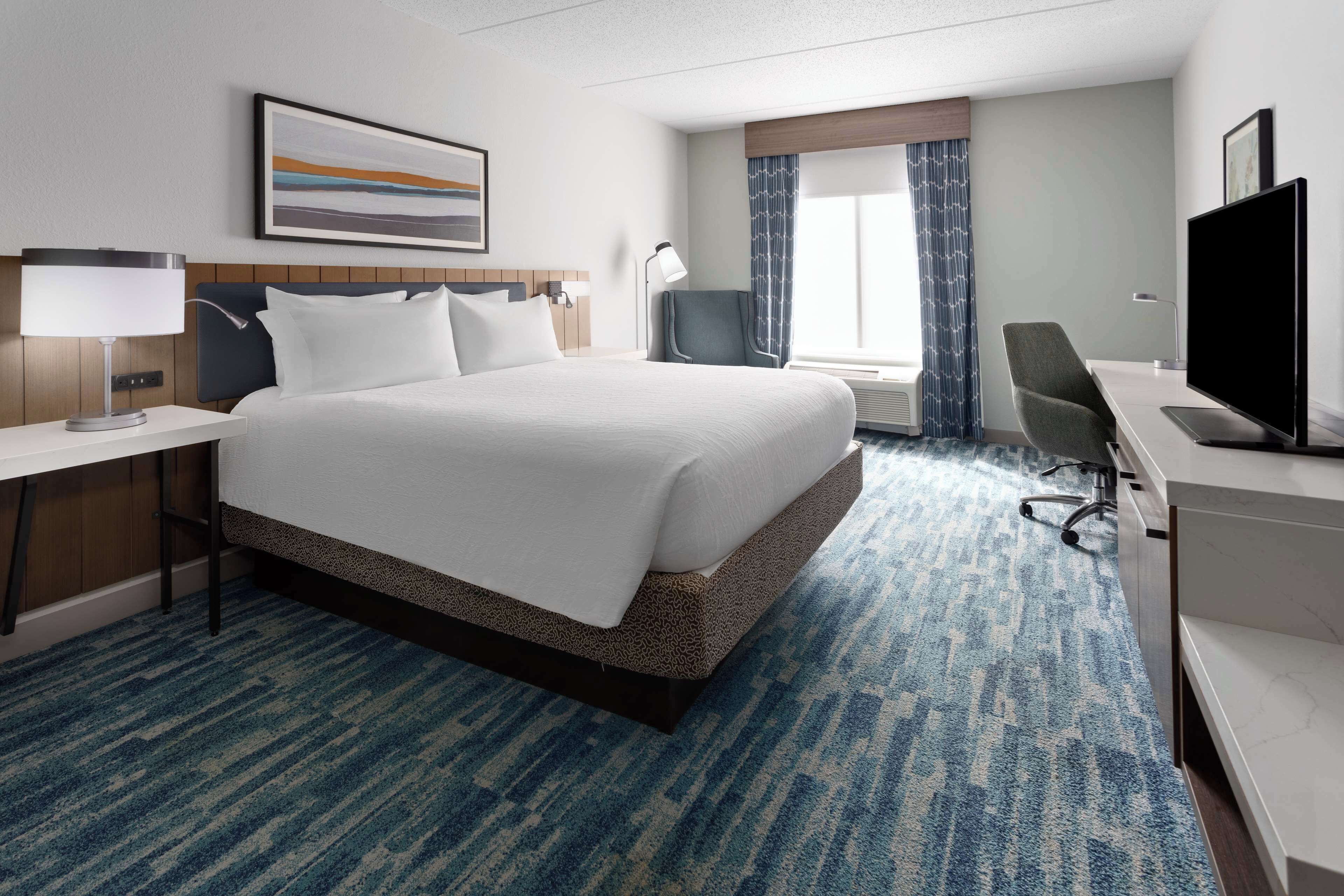A hotel room with a large bed, a desk with a computer, a chair, and a TV.