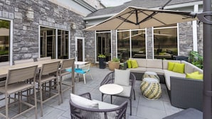 Un espace extérieur aménagé en terrasse, avec des murs en pierre, un coin salon couvert et divers types de sièges, notamment des tables et des chaises.