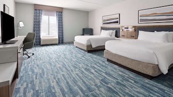 A hotel room with two beds, a desk with a computer, a chair, and a large window with curtains.