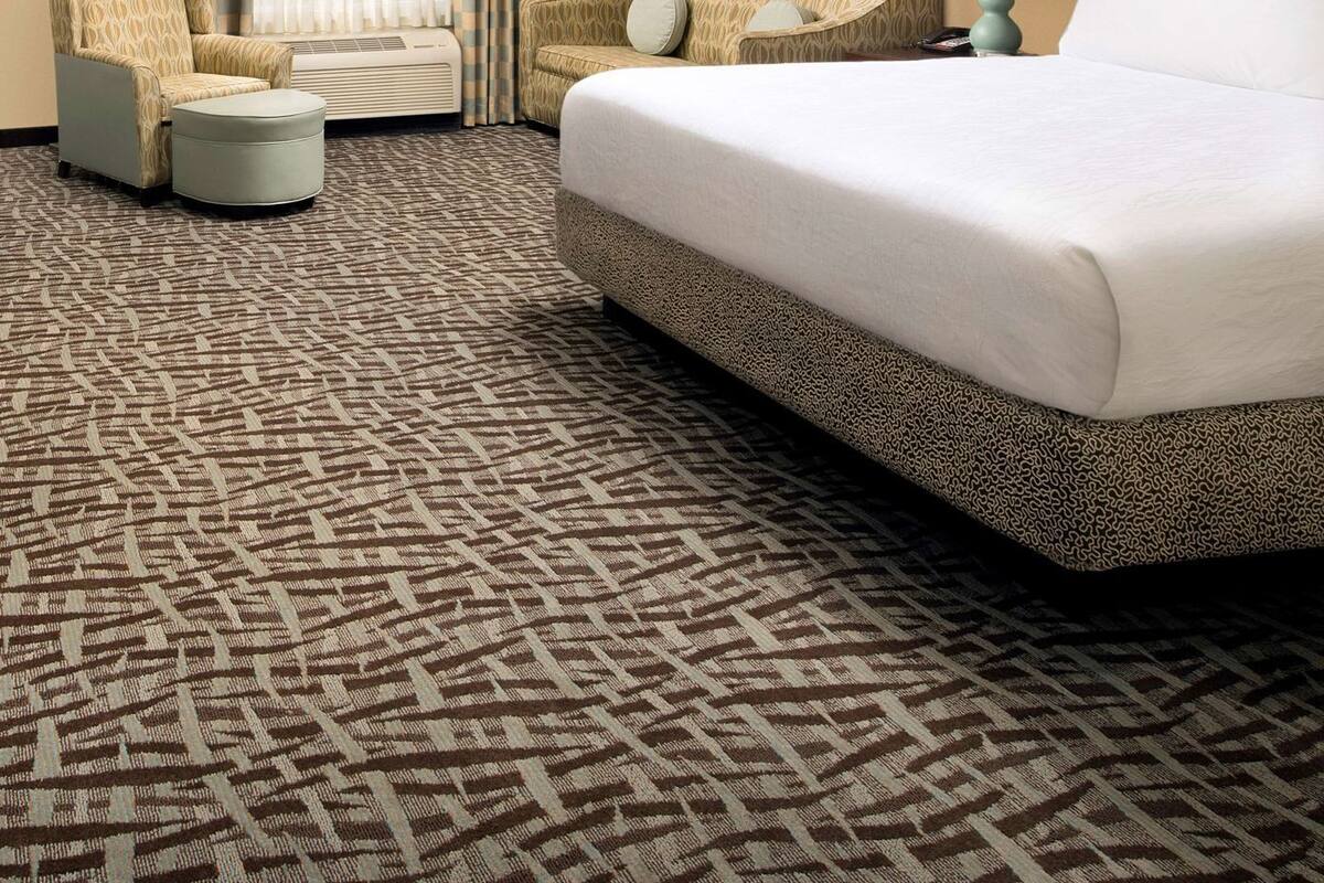 Ein Hotelzimmer mit einem großen Bett, zwei Sesseln, einem kleinen Tisch und einem gemusterten Teppich.