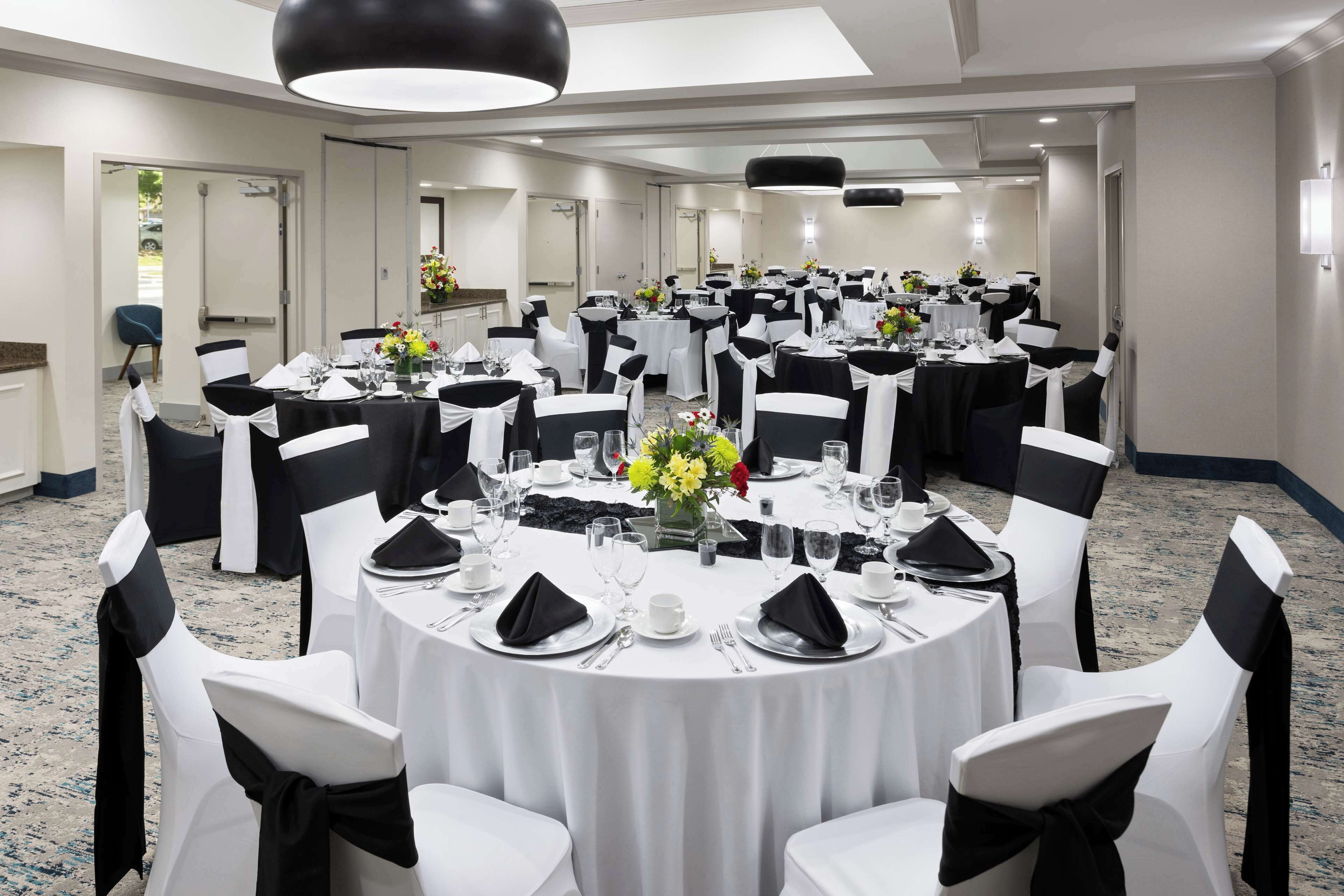 A banquet hall with round tables set for dining, white chairs with black sashes, and a chandelier.