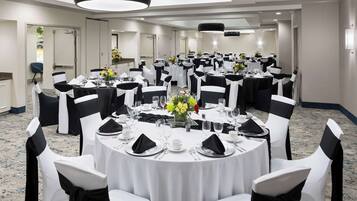 A banquet hall with round tables set for dining, white chairs with black sashes, and a chandelier.