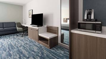 A hotel room with a sofa, a desk with a flat-screen TV, a coffee machine, and a large mirror.