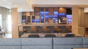 Un moderno vestíbulo de hotel con área de bar, disposición de asientos y una mesa de recepción.
