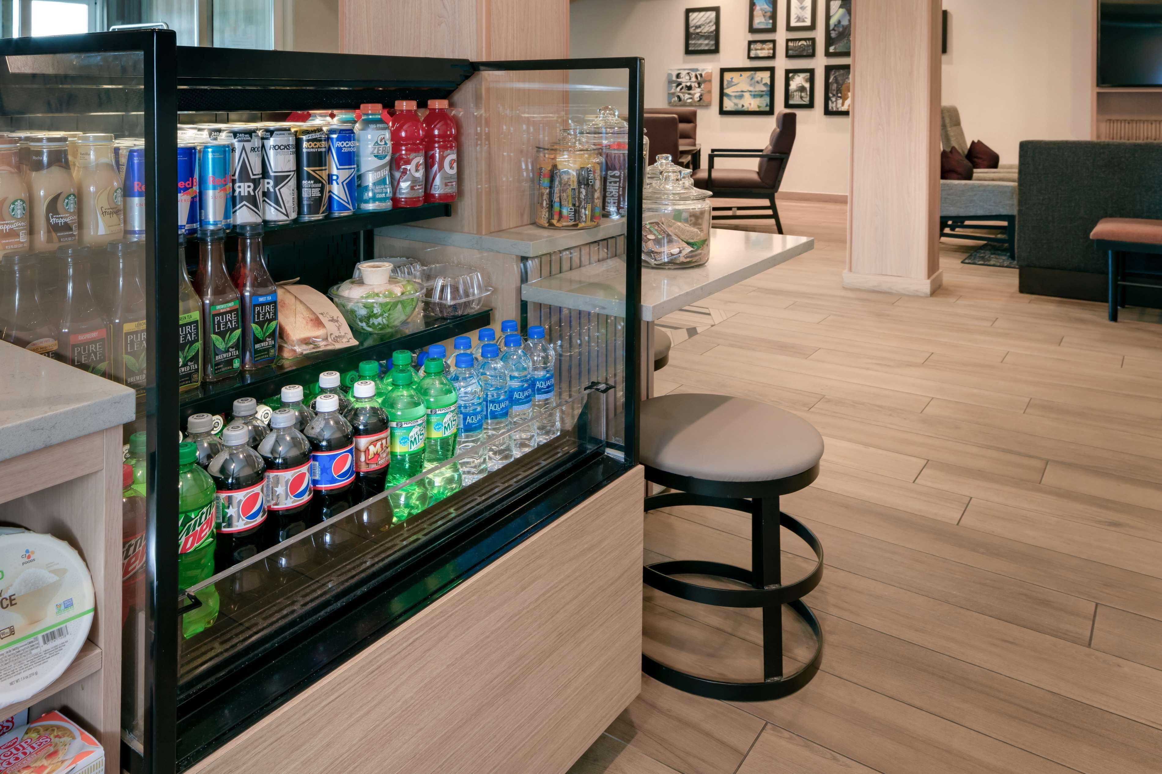 A beverage refrigerator stocked with various drinks, a seating area with a bar stool, and a wooden floor.