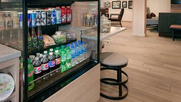 A beverage refrigerator stocked with various drinks, a seating area with a bar stool, and a wooden floor.