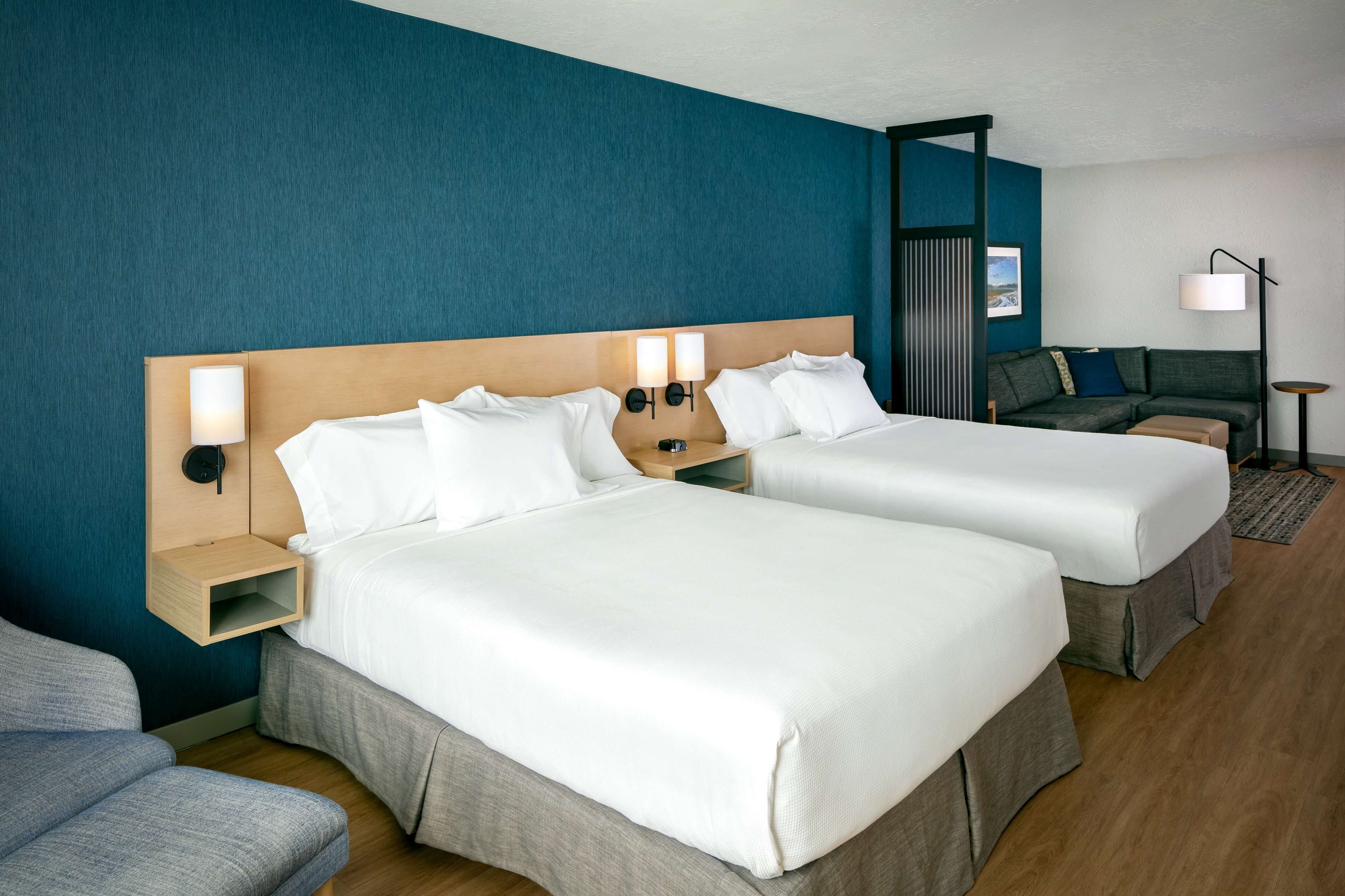 A hotel room with two beds, a sofa, a nightstand, and a lamp.