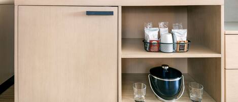 A wooden cabinet with a TV above it, containing kitchen items like a pot, cups, and glasses.