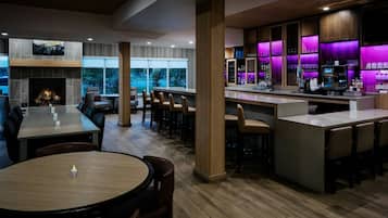 A modern restaurant with a bar area, wooden flooring, and a fireplace.