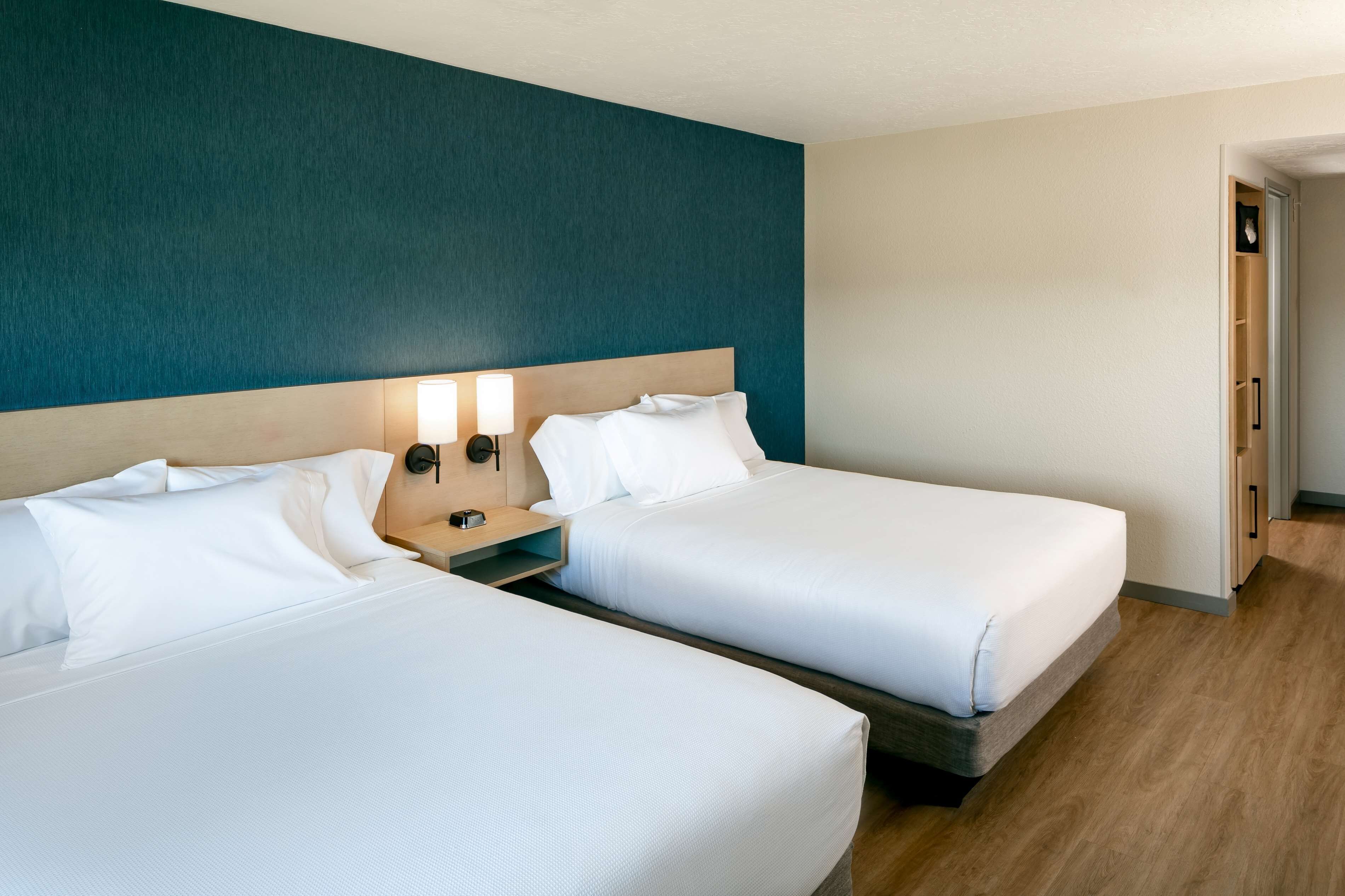 A hotel room with two beds, a wooden headboard, and a teal accent wall.