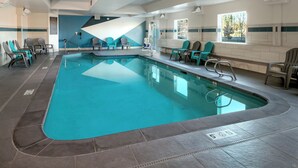 Una piscina con sillas alrededor, suelo de baldosas y una ventana con vistas a árboles.