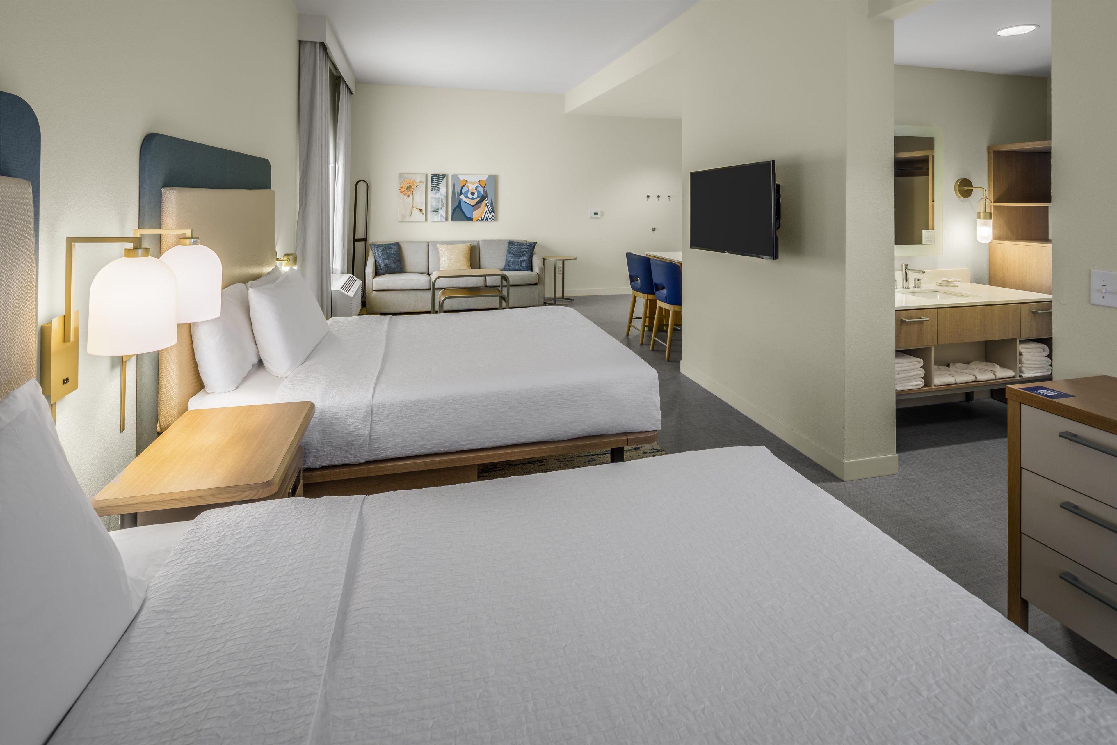 A hotel room with two beds, a desk, a chair, a TV, and a bathroom.