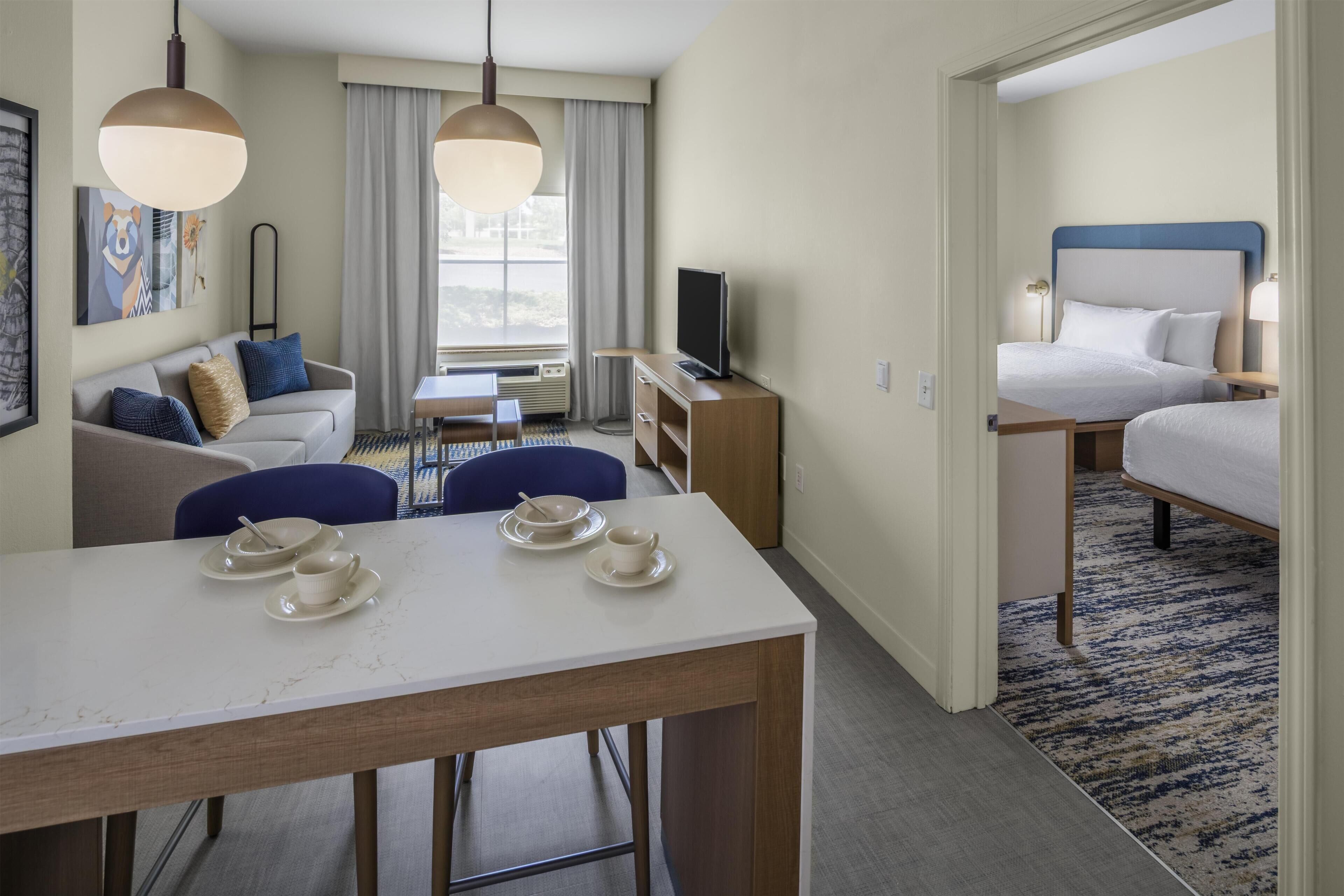 A hotel room with a dining table, a sofa, a TV, and a bed.