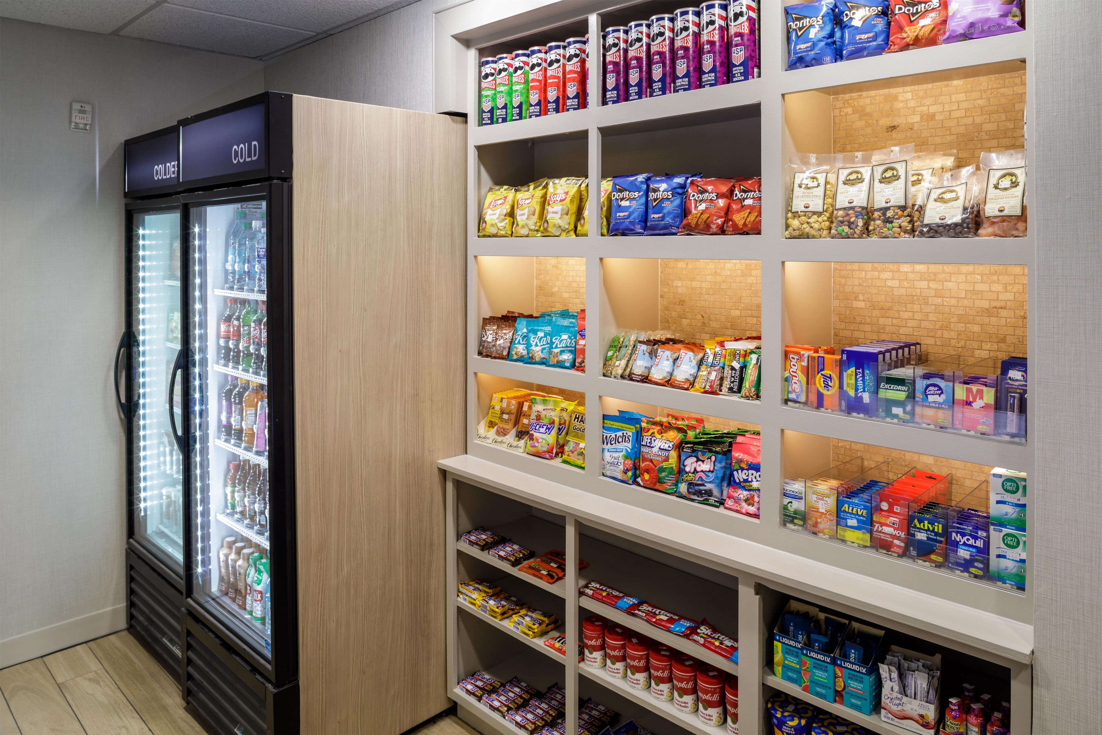 En kylskåpsliknande dryckesautomat, hyllor med snacks och ett stort utbud av förpackade varor i en butik.