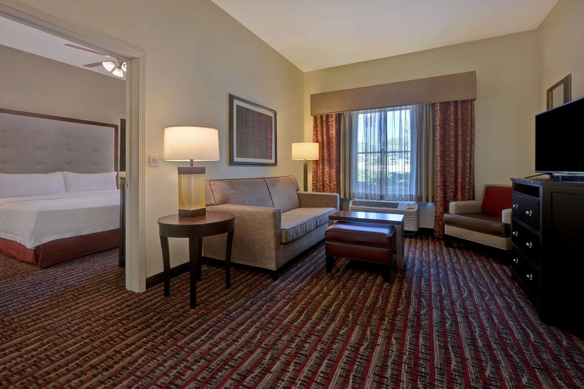 A hotel room with a bed, a sofa, a coffee table, a TV, and a window with curtains.