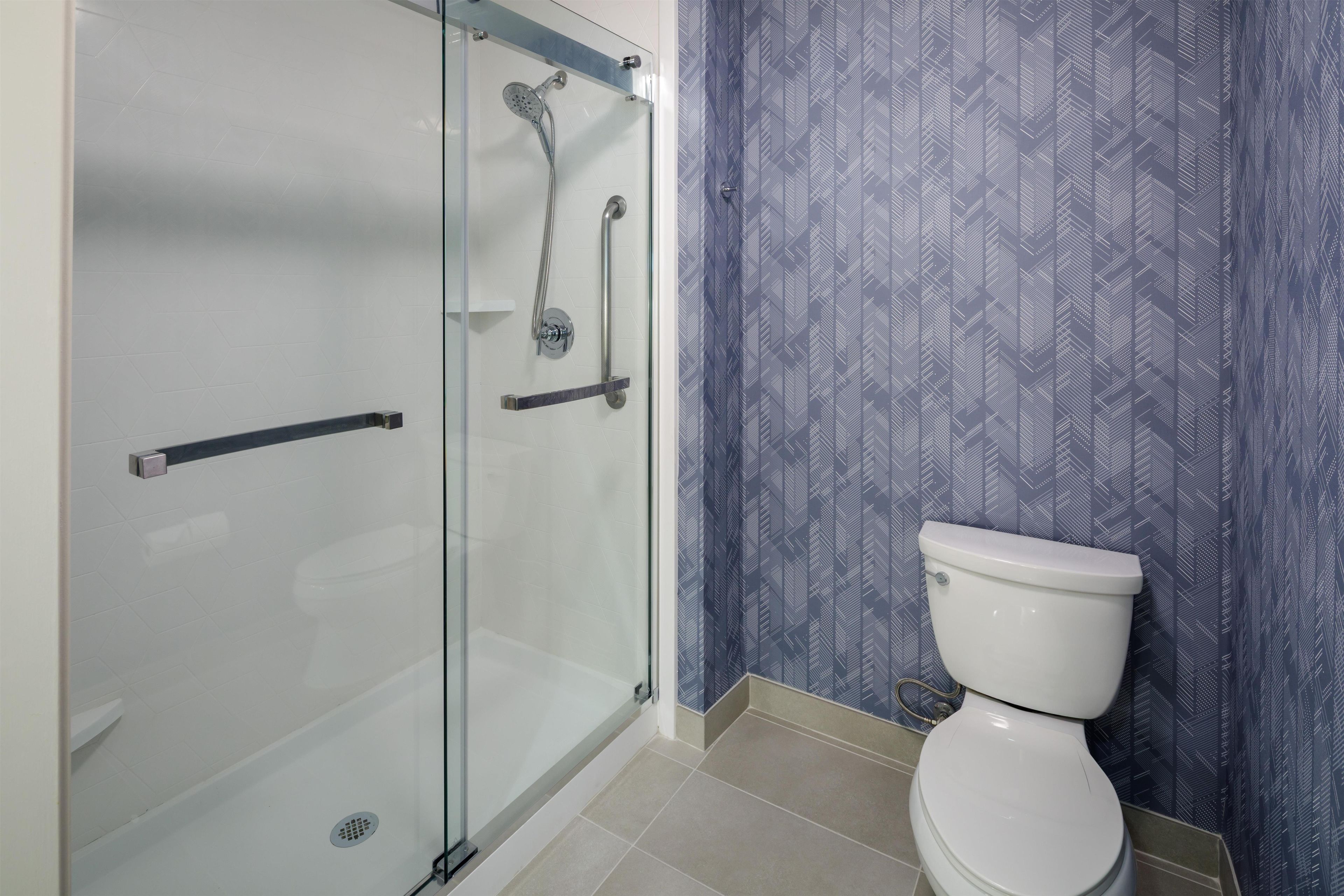 Une salle de bain avec une douche à parois de verre, des toilettes et un papier peint à motifs.