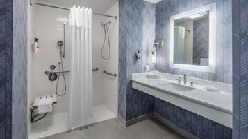 A modern bathroom with a shower, a large mirror, and a vanity with two sinks.