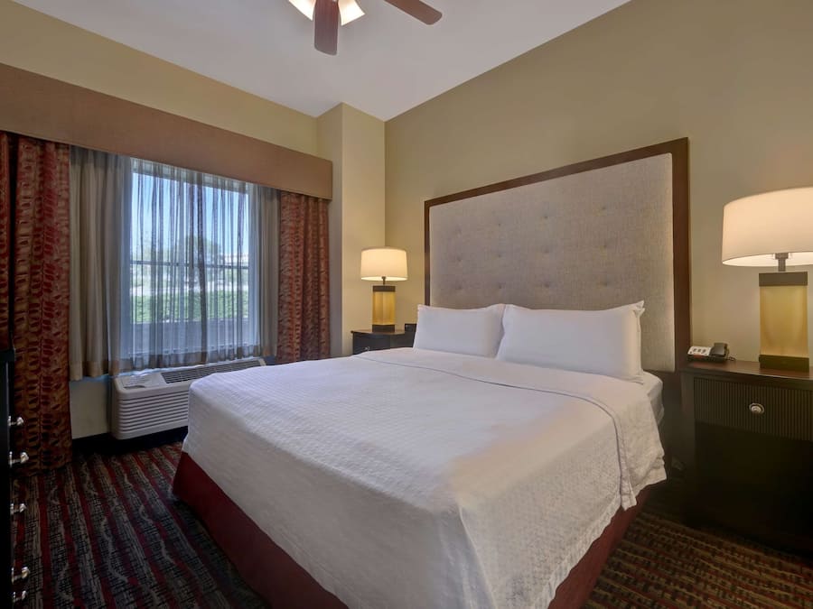 A hotel room with a large bed, two bedside lamps, a heater, and a window with curtains.