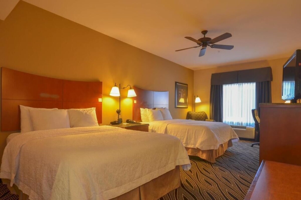 Una habitación de hotel con dos camas, ventilador de techo, escritorio y televisor.