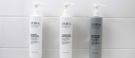 Trois bouteilles de shampoing, d’après-shampoing et de gel douche « ZERO % », posées contre un mur recouvert de carreaux blancs.