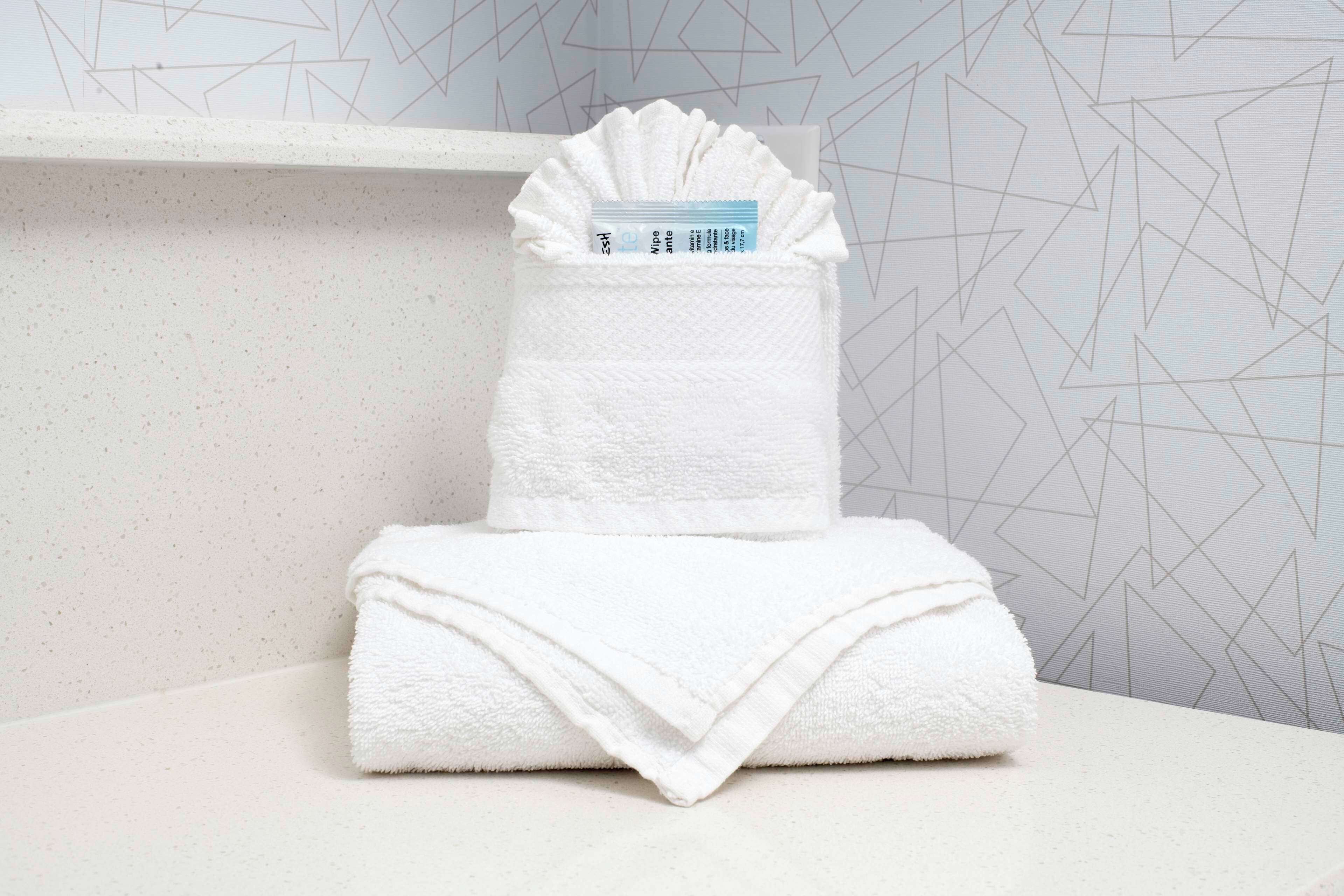 A neatly folded white towel stacked on a white surface with a geometric patterned wall in the background.