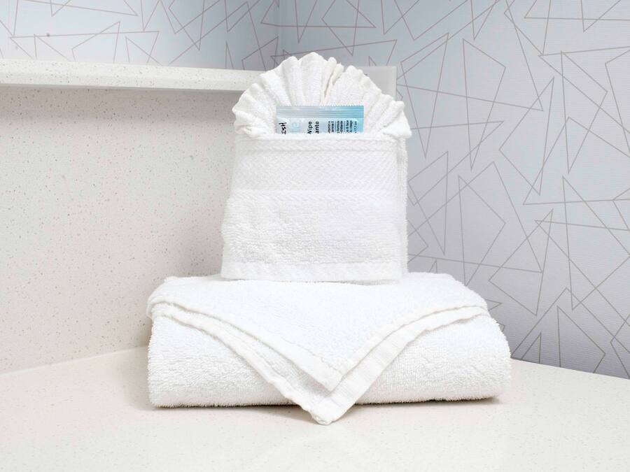 A neatly folded white towel stacked on a white surface with a geometric patterned wall in the background.