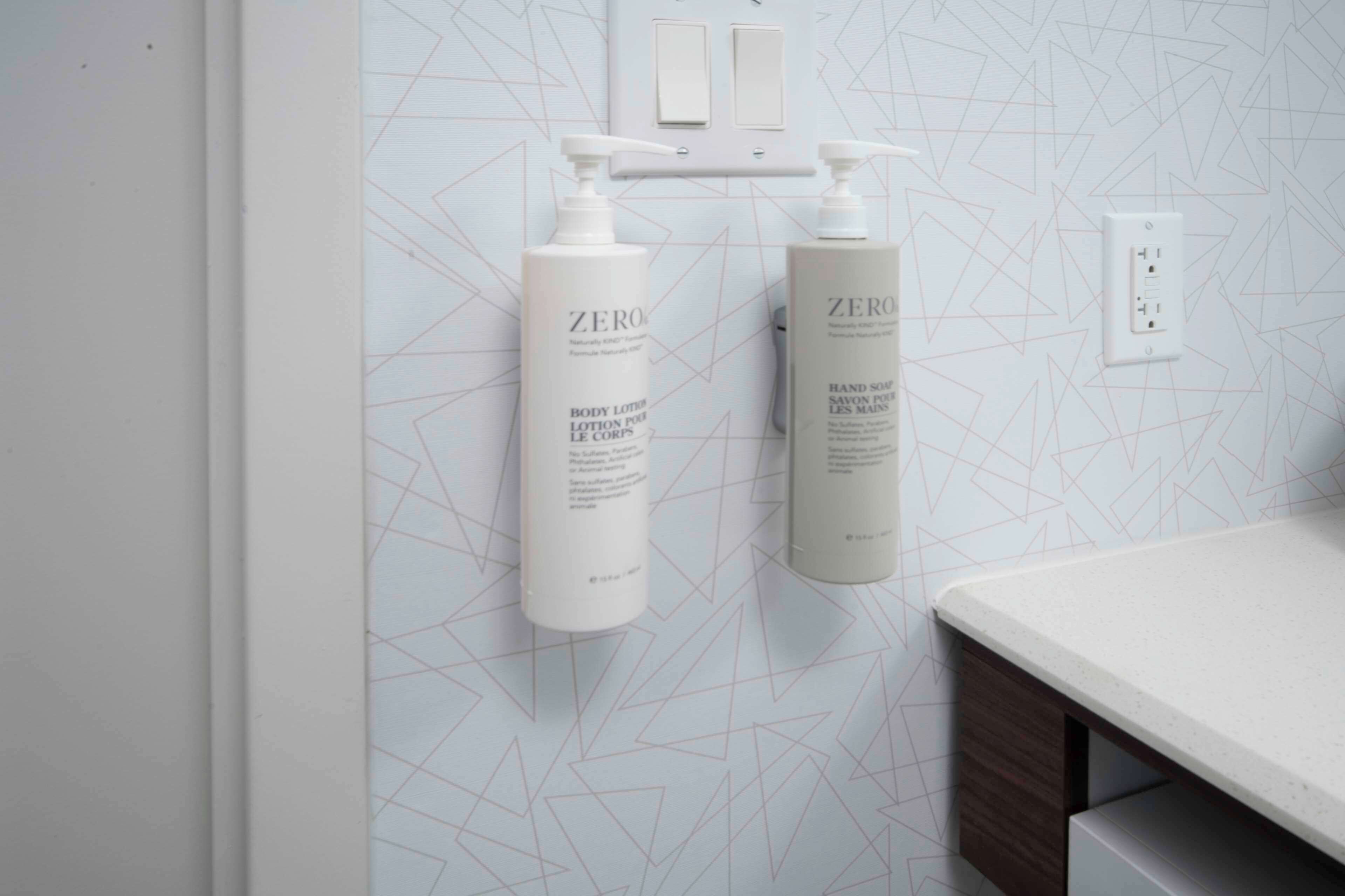A bathroom with a geometric patterned wall, two white bottles of Zero body lotion, and a white countertop.