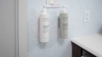 A bathroom with a geometric patterned wall, two white bottles of Zero body lotion, and a white countertop.