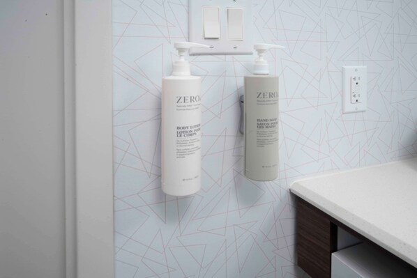 A bathroom with a geometric patterned wall, two white bottles of Zero body lotion, and a white countertop.
