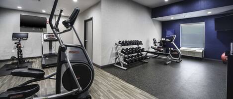 Une salle de sport équipée de tapis de course, de vélos elliptiques et d’une série de haltères.