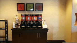 A coffee station with multiple coffee dispensers, a small shelf with condiments, and a framed artwork on the wall. - Hampton Inn Topeka (Topeka)