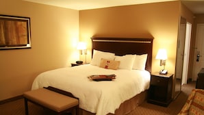 A hotel room with a large bed, two bedside tables, a bench, and a chair. - Hampton Inn Topeka (Topeka)