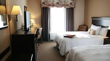 A hotel room with a bed, a desk with a lamp, a television, and a window with curtains.