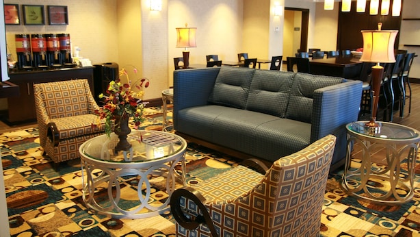A hotel lobby with a patterned carpet, a blue sofa, patterned chairs, a coffee station, and a dining area. - Hampton Inn Topeka (Topeka)