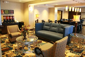 Relax in our inviting lobby, featuring a cozy seating area with a sofa and armchairs, a coffee station, and a beautiful vase with flowers.