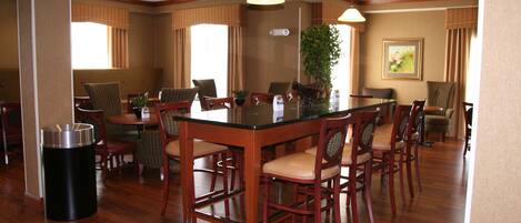 A hotel dining area with wooden flooring, a central island table, and multiple dining tables with chairs.