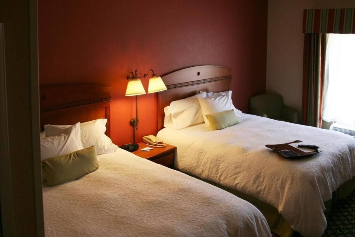 A hotel room with two beds, a nightstand with a lamp, a telephone, and a window with curtains.