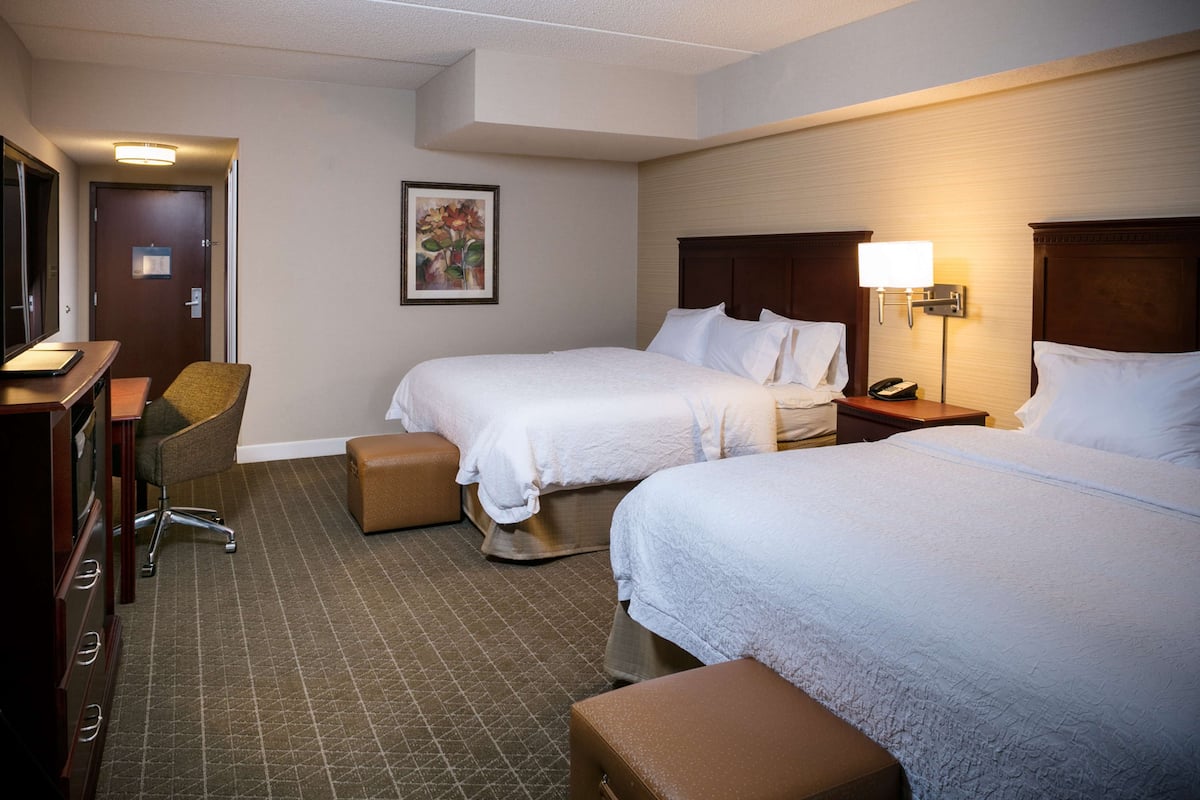 A hotel room with two beds, a desk, a chair, and a small table.