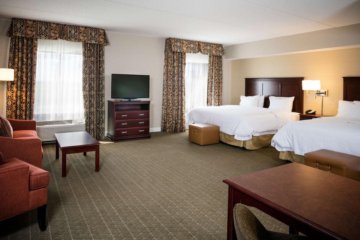 A hotel room with two beds, a TV, a desk, a chair, and a sofa.