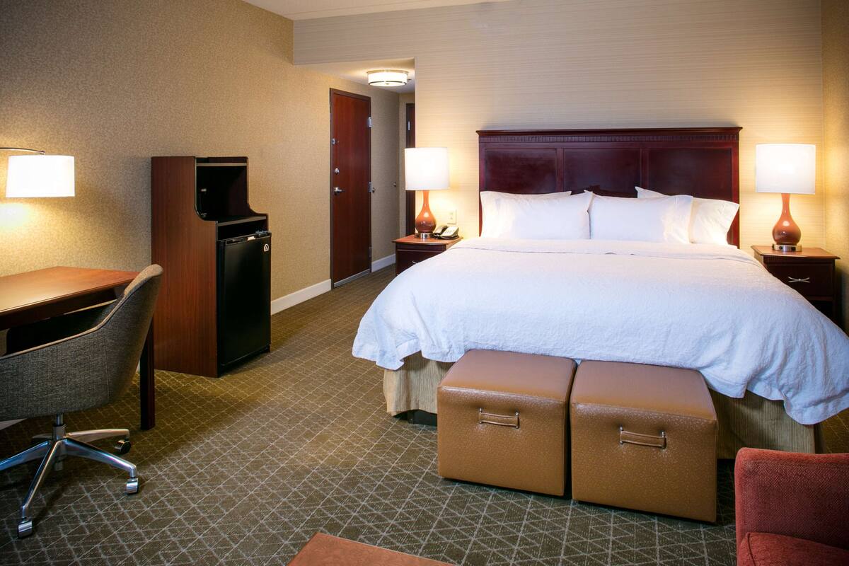 A hotel room with a bed, desk, chair, and a minibar.