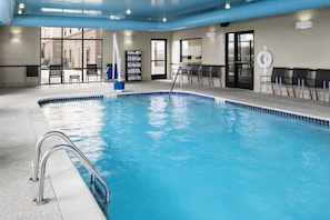 Una piscina con agua cristalina y azul, rodeada de sillas de descanso y un puesto de socorristas.