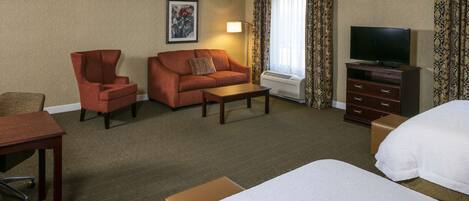 A hotel room with a bed, a sofa, a chair, a desk, a television, and a window with curtains.