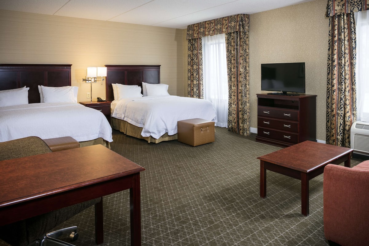 A hotel room with two beds, a desk, a dresser, and a television.