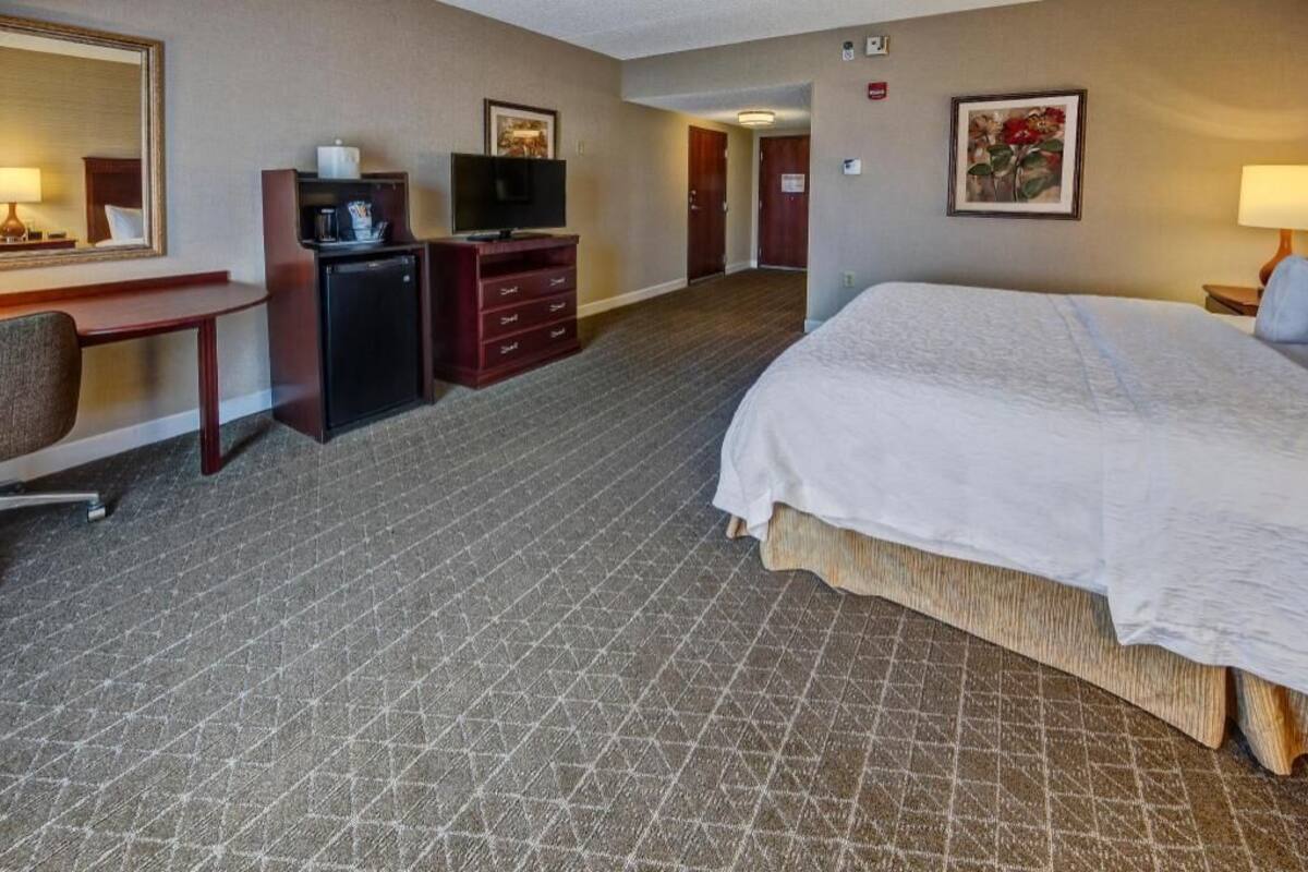 A hotel room with a bed, desk, TV, and dresser.