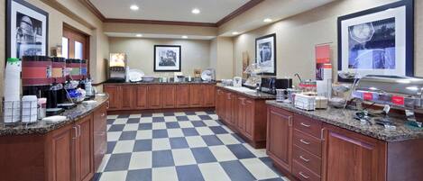 A hotel kitchen with checkered flooring, wooden cabinets, and various food service equipment.