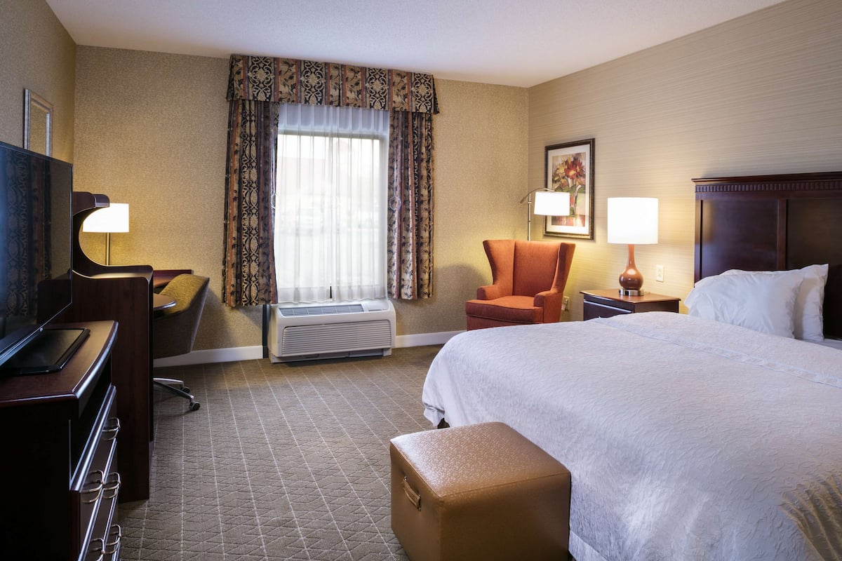 A hotel room with a bed, a desk with a computer, an air conditioner, a chair, and a television.