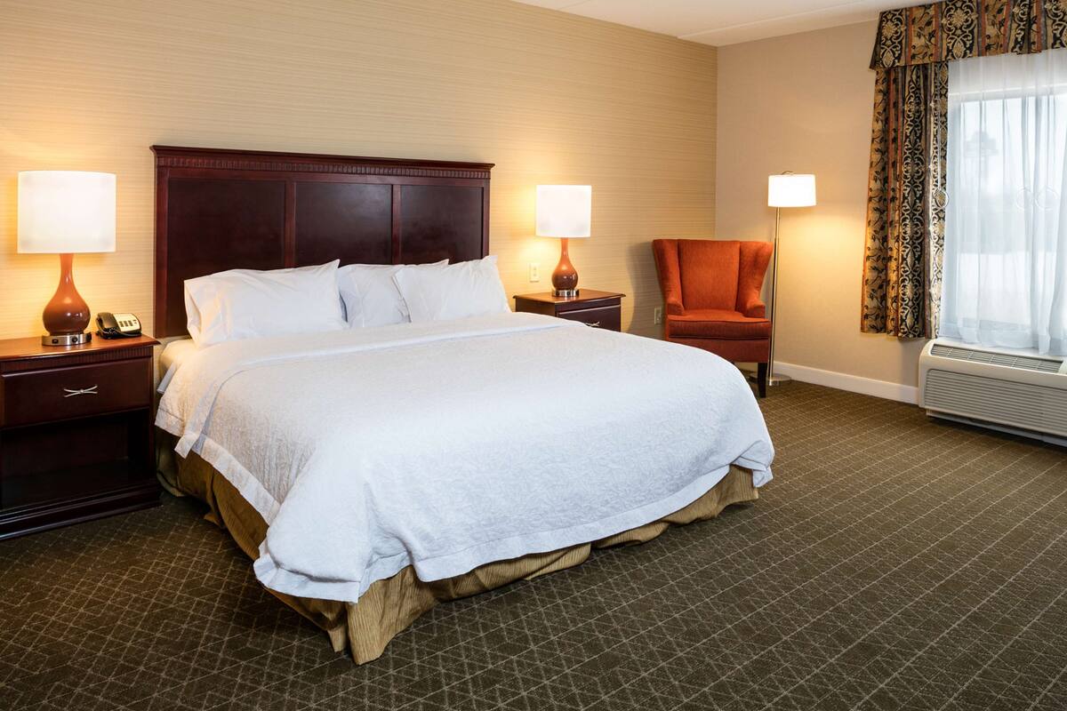 A hotel room with a large bed, two bedside tables with lamps, a chair, and a window with curtains.